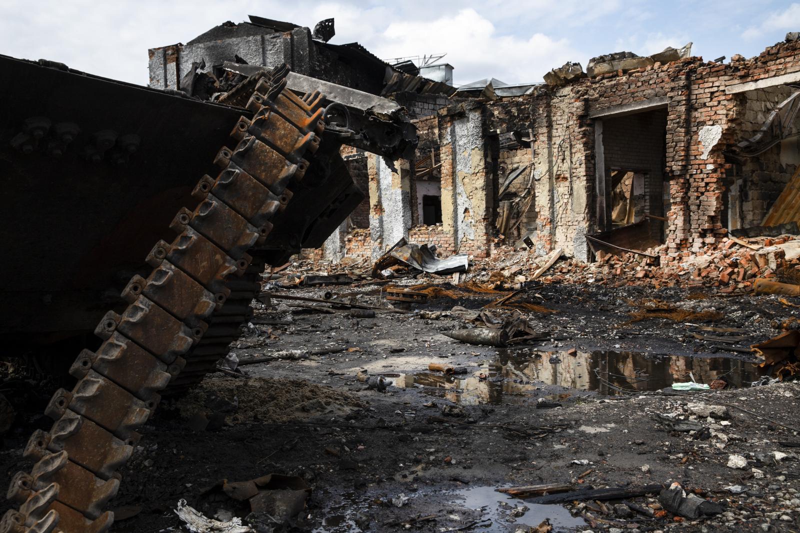 In primo piano i rottami arrugginiti di un carrarmato, con i cingoli in evidenza; sullo sfondo rovine di abitazioni devastate dalla guerra