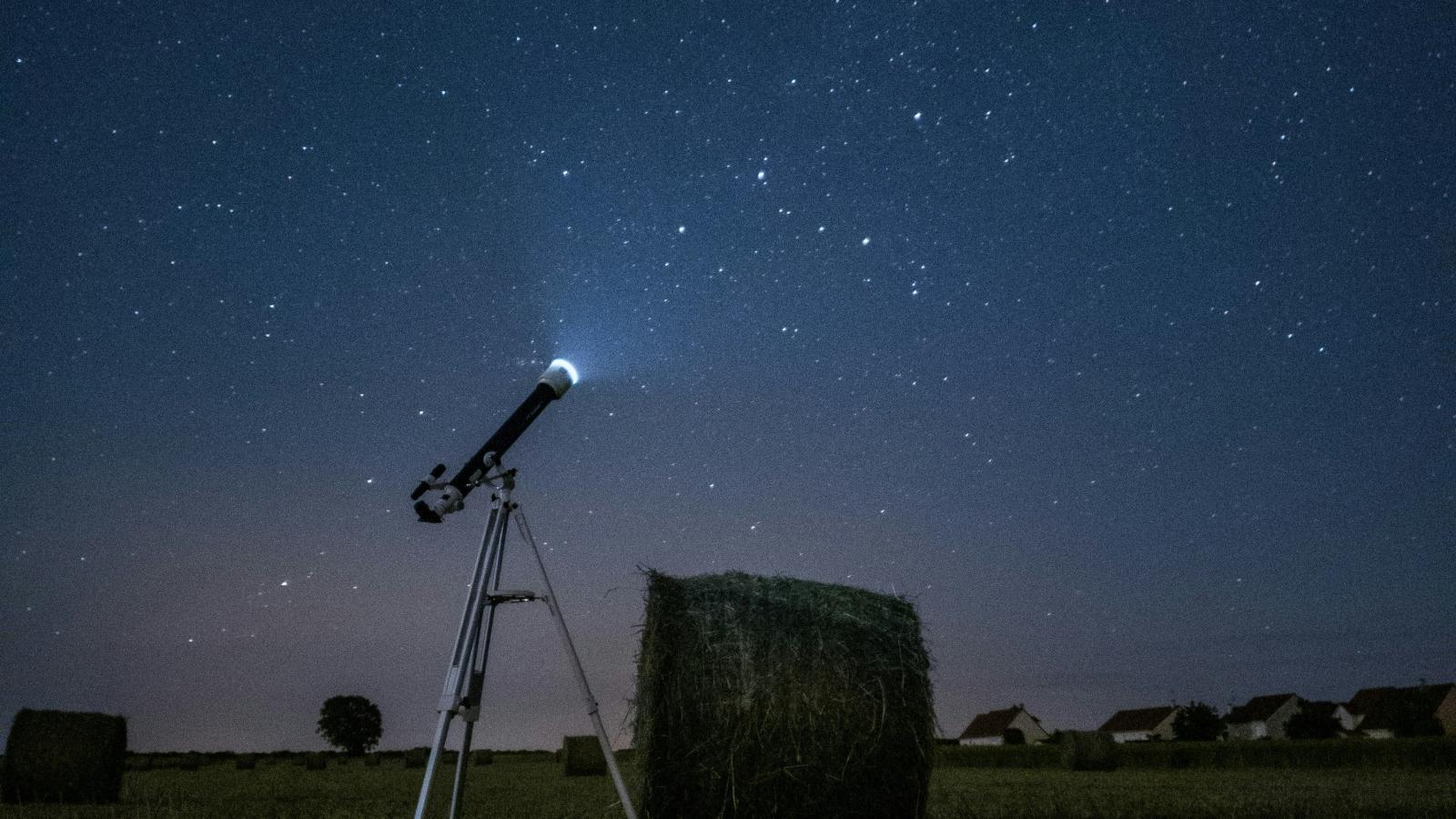 In un prato, di notte, un telescopio che emette luce punta verso il cielo stellato