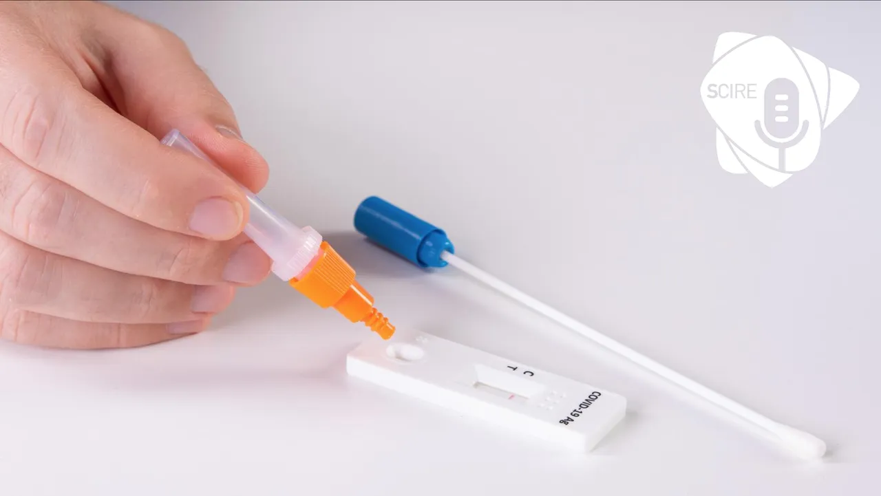 Una mano versa con una provetta arancione alcune gocce su un test antigenico rapido, accanto a un tampone, su fondo bianco.
