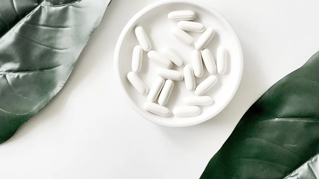 Un piattino pieno di compresse di un farmaco bianco tra due foglie verdi