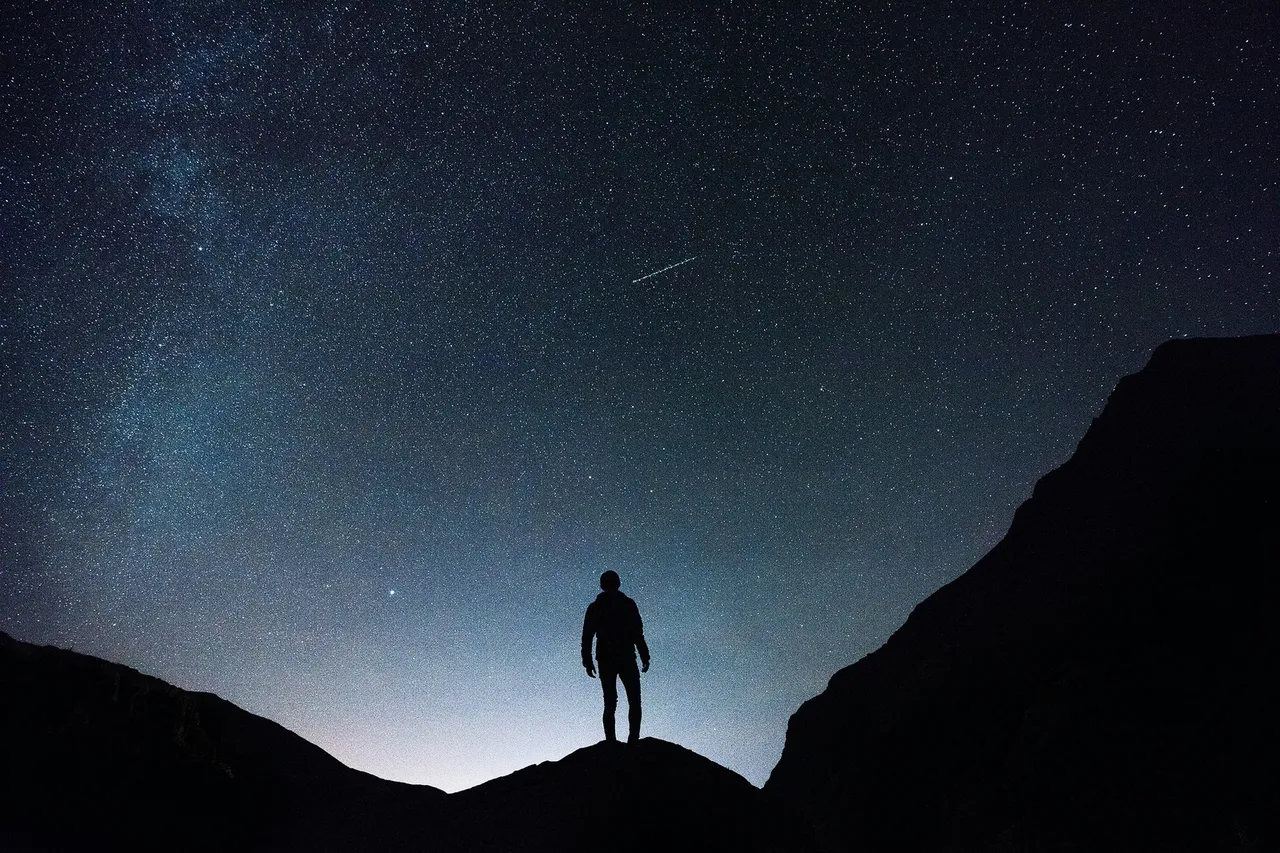 Silhouette di un uomo in un paesaggio di montagna di notte sullo sfondo del cielo stellato