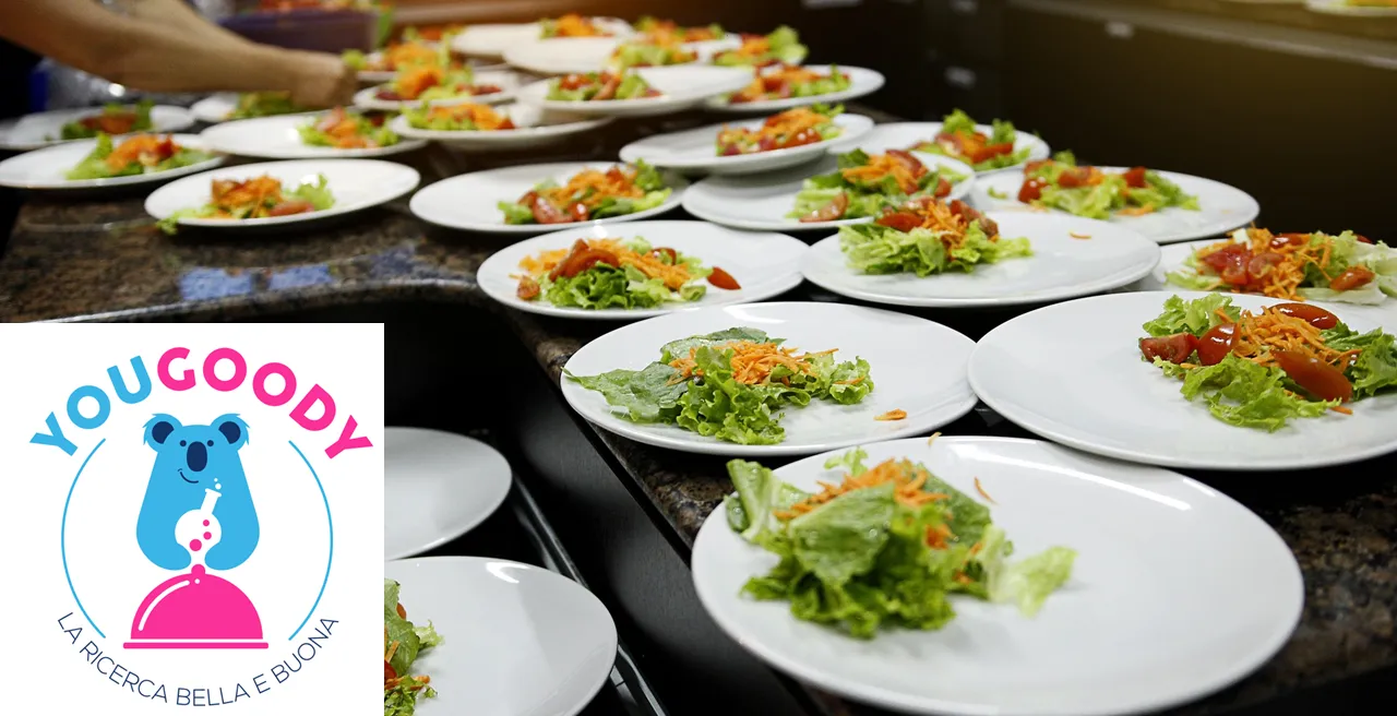 Una tavolata di piatti contenenti insalata e il logo YouGoody - la ricerca bella e buona in sovraimpressione
