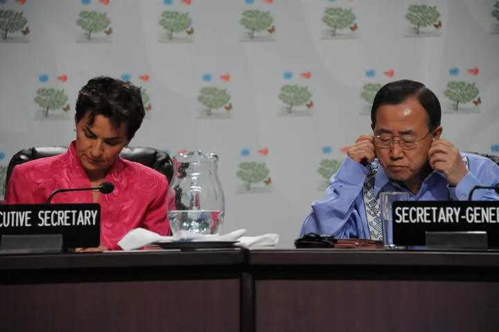 Christiana Figueres e Ban Ki-moon seduti al tavolo della presidenza alla COP16 di Cancún; lui si sistema l'auricolare della traduzione.