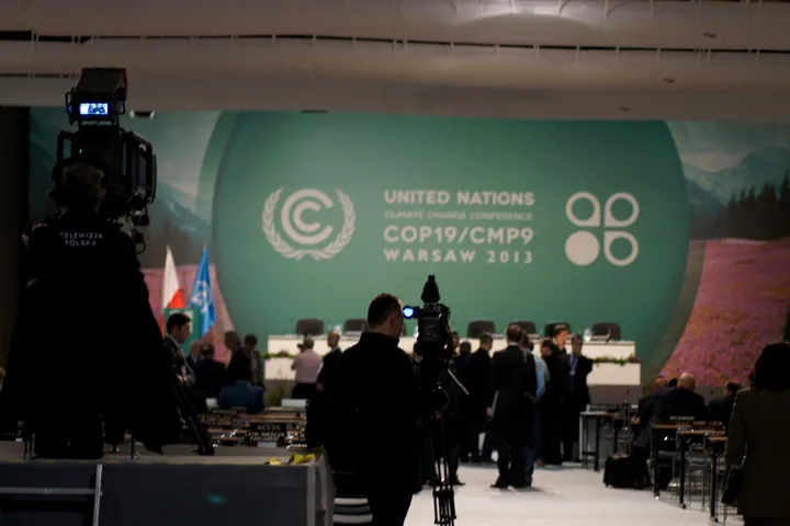 La sala della plenaria della COP19 allo Stadio nazionale di Varsavia, con operatori e telecamere davanti al palco e il logo della conferenza.