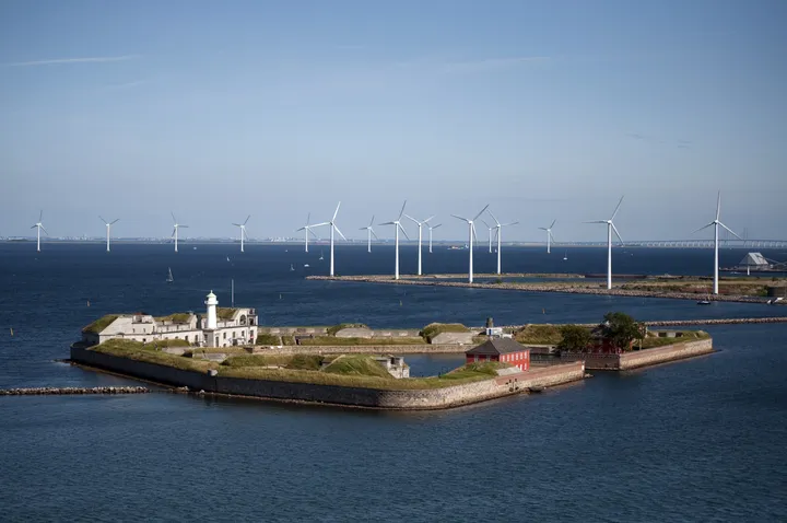 Una fila di turbine eoliche in mare al largo di Copenaghen, dietro un'isola fortificata.