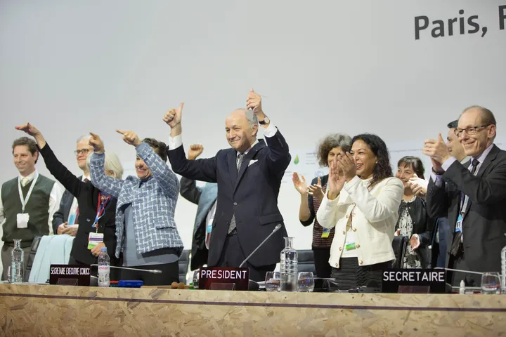 Laurent Fabius e gli altri al tavolo della presidenza alzano le braccia dopo l'adozione dell'Accordo di Parigi, il 12 dicembre 2015.