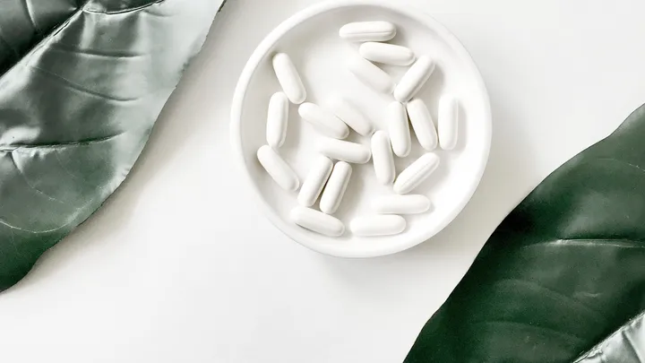Un piattino pieno di compresse di un farmaco bianco tra due foglie verdi
