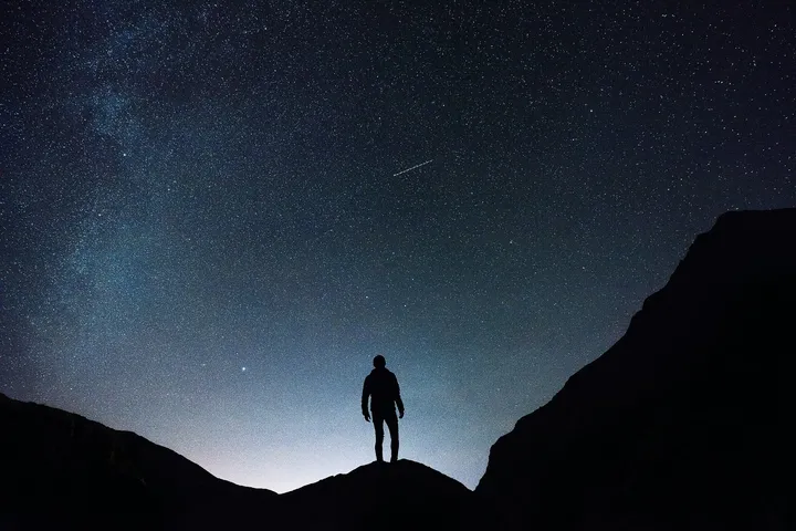 Silhouette di un uomo in un paesaggio di montagna di notte sullo sfondo del cielo stellato